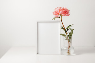 White wooden picture frame mockup with peony flower in the vase on the white wooden table. Photo...