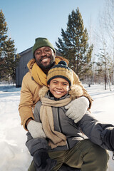 Happy young African American man and his cute son in warm winterwear taking selfie and looking at camera on winter weekend