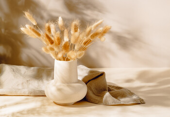 Vase with lagurus dried grass bouquet and linen towel, aesthetic sunlight shadows. Ceramic vase...