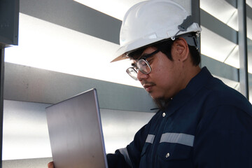 Chief engineer in hard hat walks through modern factory lighting while holding laptop. Successful handsome man in modern industrial environment.