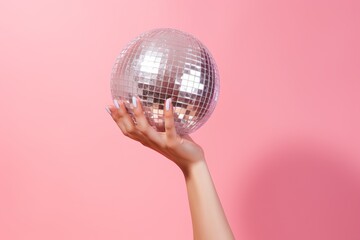 Women's hand holding disco ball on pink background. Season's greetings concept. Sunbeam on the pink. Flat lay and copy space

