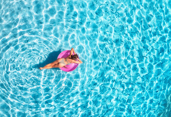 Aerial view of a young woman swimming with pink swim ring in blue sea with school of fish at sunset in summer. Tropical landscape with girl, clear azure water, sandy beach in Greece. Top view. Travel