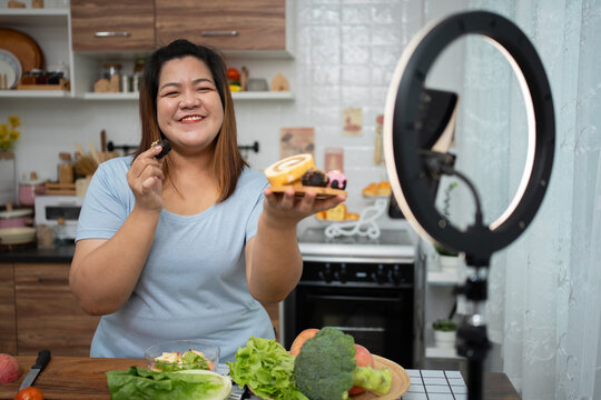 Asian Pregnant blogger looking at smartphone camera, she is live streaming cooking class for pregnant. Asian woman standing happily smiling at the kitchen counter preparing fresh organic salad.