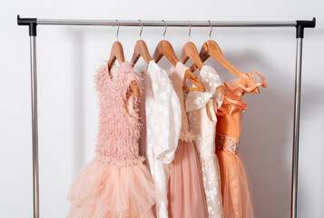 Puffy dresses hang on hanger on clothes rail on white wall background.