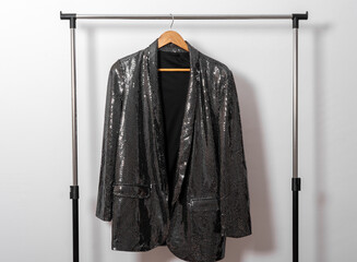 Shiny jacket hangs on hanger against white wall. Rental  clothing concept.