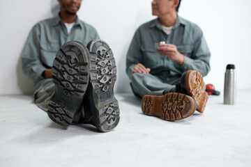 Boot soles of builders sitting on floor and eating lunch at construction site