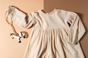 Top view flat lay linen kids dress with wooden horse toy on beige and brown background. Eco...
