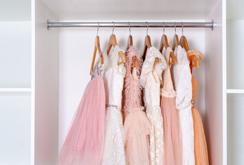 Assortment of children's dresses and skirts made of lush organza hangs in white wardrobe.