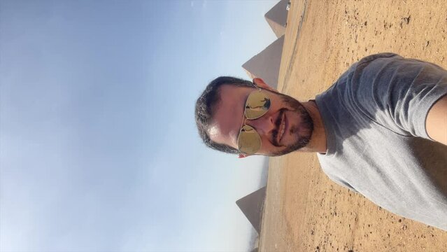 Tourist man makes victory sign with the pyramids of Giza in the background, Egypt. Achievement, satisfaction. Vertical
