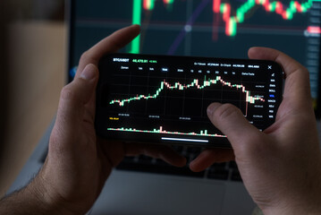 Smartphone with mobile application cryptocurrency wallet. A man analyzes the price chart for...