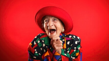 Saying WOW, a happy fisheye portrait caricature of funny elderly woman with red hat isolated on red...