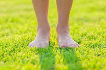 Young adult woman barefoot standing on fresh green grass at park in beautiful warm sunny summer...