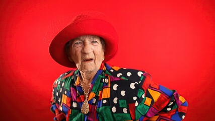 Portrait of concerned, unhappy elderly senior old funny crazy woman with wrinkled skin red hat and...
