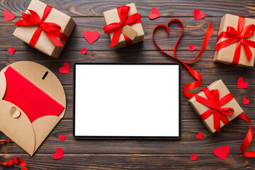 Fototapeta premium Top view of digital tablet with gift boxes and hearts on colorful background. Tablet with black screen with Holiday decorations gift box top view