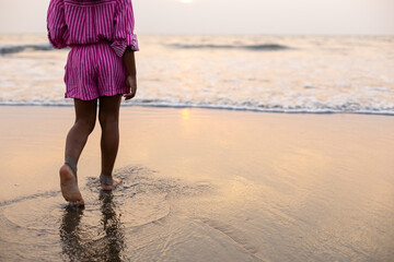 Layout for postcard. Unrecognizable girl walks barefoot through water to waves at sunset on beach.