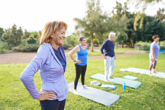 Multiracial senior people doing workout exercises outdoor with city park in background - Healthy lifestyle and joyful elderly lifestyle concept - Focus on latin woman face