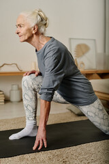 Side view of mature active woman looking forwards while standing on mat with one leg bend in knee and the other one stretched backwards