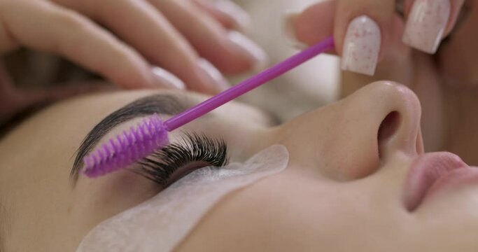 professional beautician combs the eyelashes of the client after the eyelash extension procedure. Cosmetology and skin care