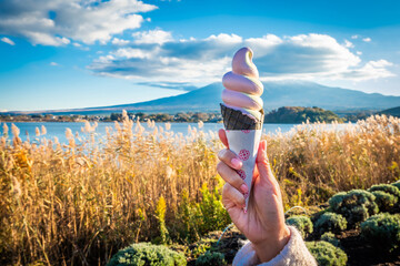 Hand holding soft serve ice cream at Lake Kawaguchiko with Mount Fuji in the background is a popular landmark among tourists.