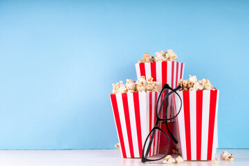 Fototapeta na wymiar Cinema, film and movie night watching concept. Clapperboard, striped popcorn bucket boxes, with glasses on light blue background, copy space