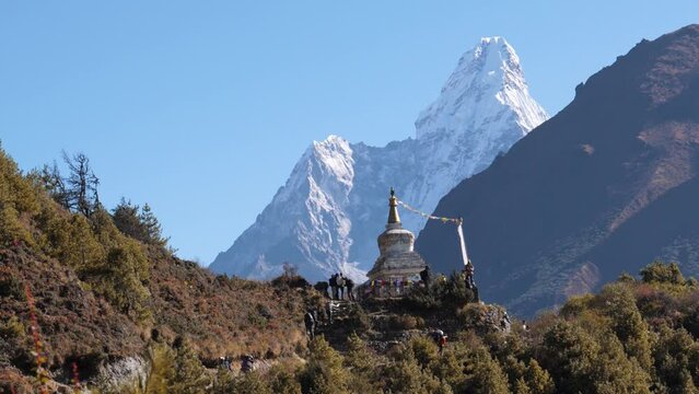 Hiking path made by sherpas in Himalayan mountains to Everest base camp trek. Organized tour groups with guides and porters with backpack walk on footpath. Nepal with snow peaks and buddhist stupa