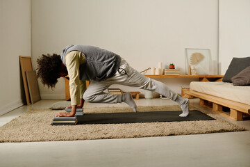 Side view of active guy in sweatpants and hoodie doing press ups against two stacks of books while...