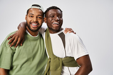 joyful african american male friends in casual wear hugging on grey background, Juneteenth
