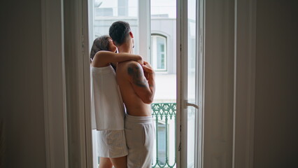 Romantic couple hugs at balcony place. Lovers looking street talking at home