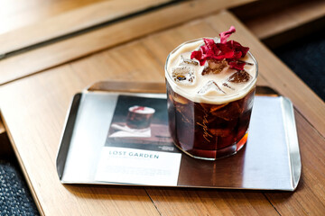 A glass of iced americano coffee ( text “ LOST GARDEN is coffee’s name)