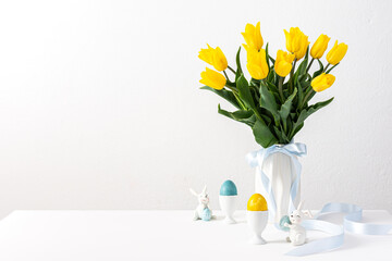 Fototapeta na wymiar Easter interior, yellow tulips in a vase and Easter eggs, cute bunnies