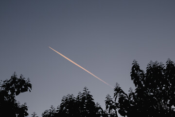 A jet plane in the blue sky. White contrail in sunset orange colors. Beautiful moment at sunset...