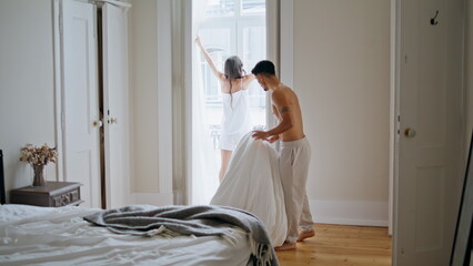 Love pair morning routine at bedroom. Woman pulling curtains watching window