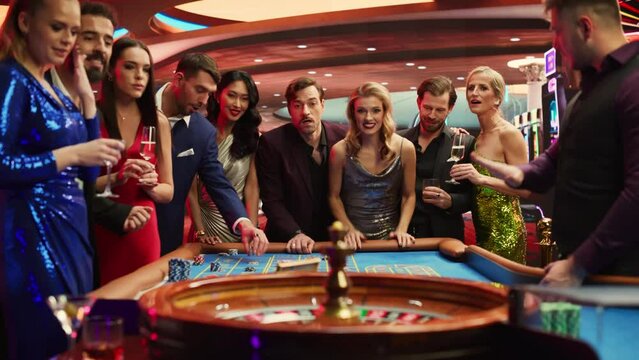 Elegantly Dressed Men and Women Enjoying Luxurious Atmosphere of a Casino. Cinematic Footage with Young People Placing Bets at the Roulette Table, Living a Lifestyle of Glamorous Entertainment.