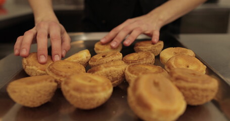 The profiteroles, which the confectioner prepares for filling with custard, are placed on a dish. Female hands of a confectioner start with eclairs.