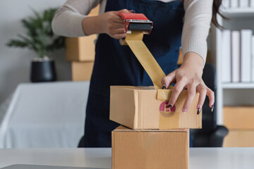 Young asian woman taping up a cardboard box in home office SME e-commerce business, relocation and...