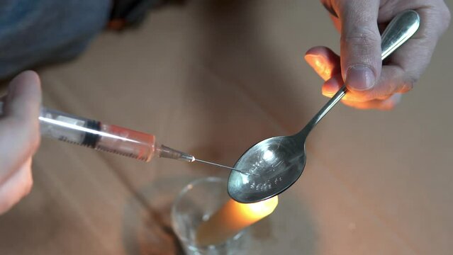 A drug addict cooks heroin on a spoon with the help of a candle fire. Drug addiction and homelessness concept.
