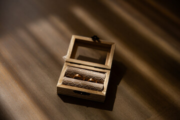 Wooden wedding rings box on a table with golden light coming through the windows. Bride and groom rings in a box.