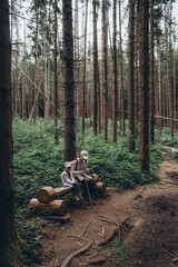 The traveler's mother and daughter sat down to rest on a bench on a mountain path among a tall coniferous forest. The mountain path goes into the distance