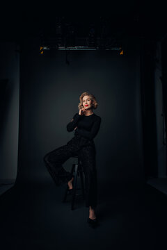 Cool Business Woman dressed i black sitting on a stol in a photo studio