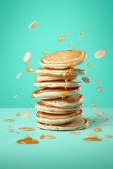  a stack of pancakes with a splash of caramel syrup on top of them on a blue and green background with a splash of caramel syrup on top of pancakes.