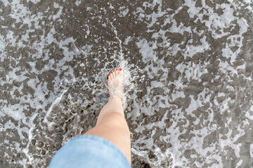 Women feet splashing and walking on the beach with red nail polish 