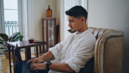 Serious guy working computer in living room close up. Focused man texting laptop