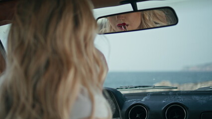 Gorgeous woman applying lipstick looking in car mirror close up. Lips makeup