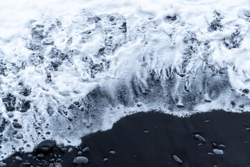 White waves crashing on a black sand beach at madeira island