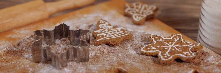 Preparation of Christmas cookies with dough rolled out on a wooden board,featuring snowflake and tree-shaped cutters.Rolling pin and sugar jar add to the festive baking scene. Banner with copy space.