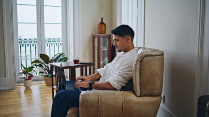 Calm man typing laptop at cozy apartment zoom on. Relaxed guy working remotely