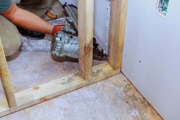 Builder is using an air hammer to nail wooden beams to housing frame
