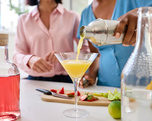 Close Up Of Female Friends At Home Having Fun Pouring Cocktails Into Glass Together