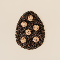 Creative composition with Easter egg shape made of roasted coffee beans and chocolate cookies on light cream background. Trendy Easter egg idea. Realistic aesthetic look. Flat lay.