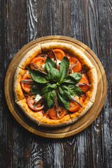 Appetizing pizza with tomatoes, anchovies and basil on a wooden background. Fluffy pizza with crispy sides.